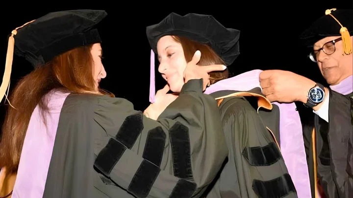 Three people participating in a doctoral hooding ceremony
