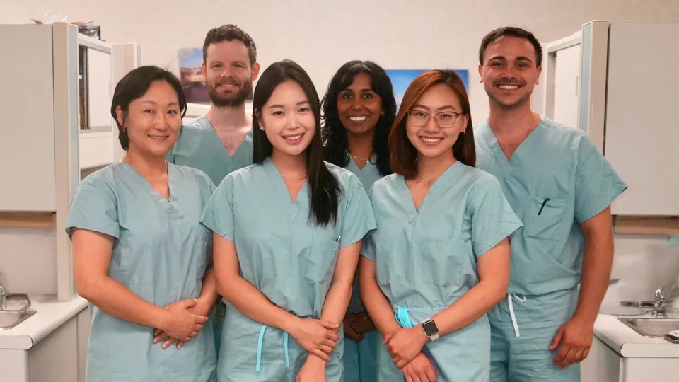 Group of six people in dental scrubs, standing in a clinic operatory