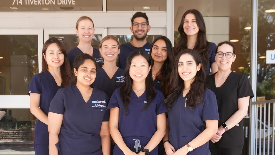 Group of 10 people in dark blue dental scrubs, standing on steps