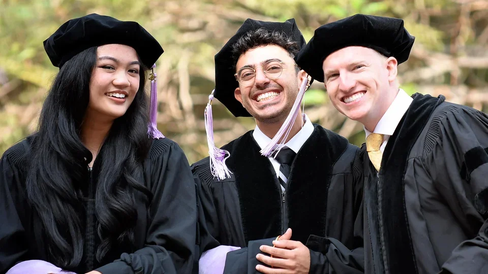Three recent dental school graduates pose for a group photo at the 2025 Commencement ceremony