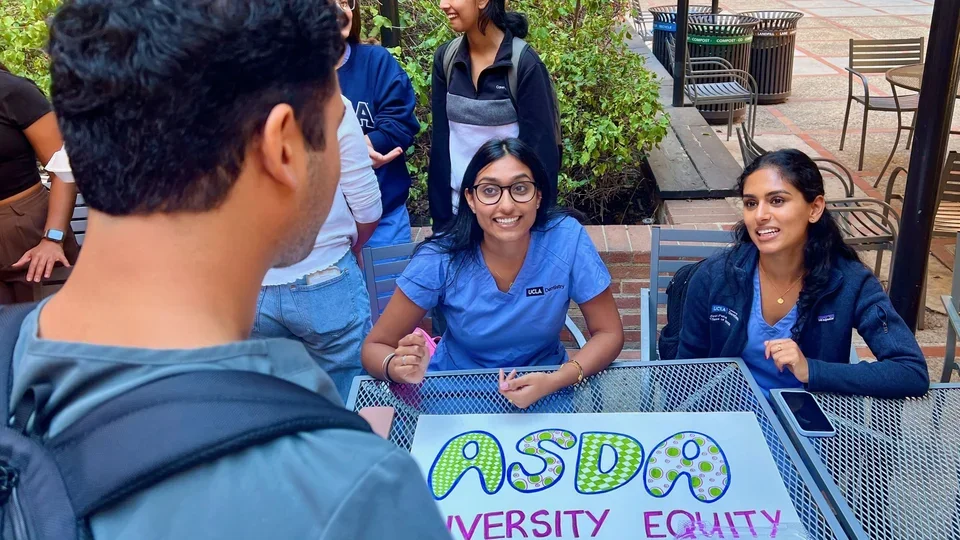 Two students sitting at a table, answering questions from another student.