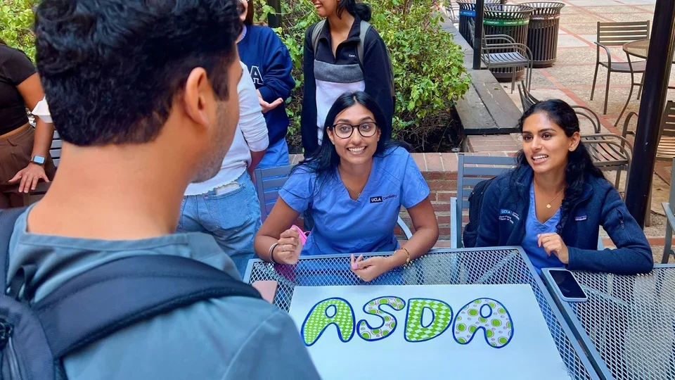 Two students speaking to another. Sign reads "ASDA"
