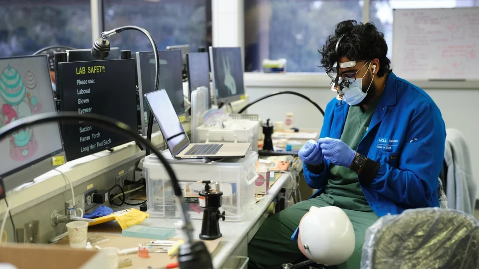 Dental students working in a simulation. lab in a blue lab coat, demonstrating proper safety techniques