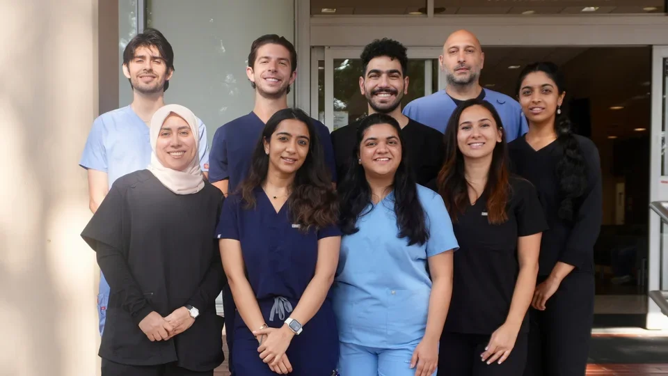 Group of nine people smiling, wearing medical scrubs