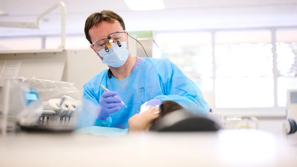 A dental student performs a clinical procedure on a patient.
