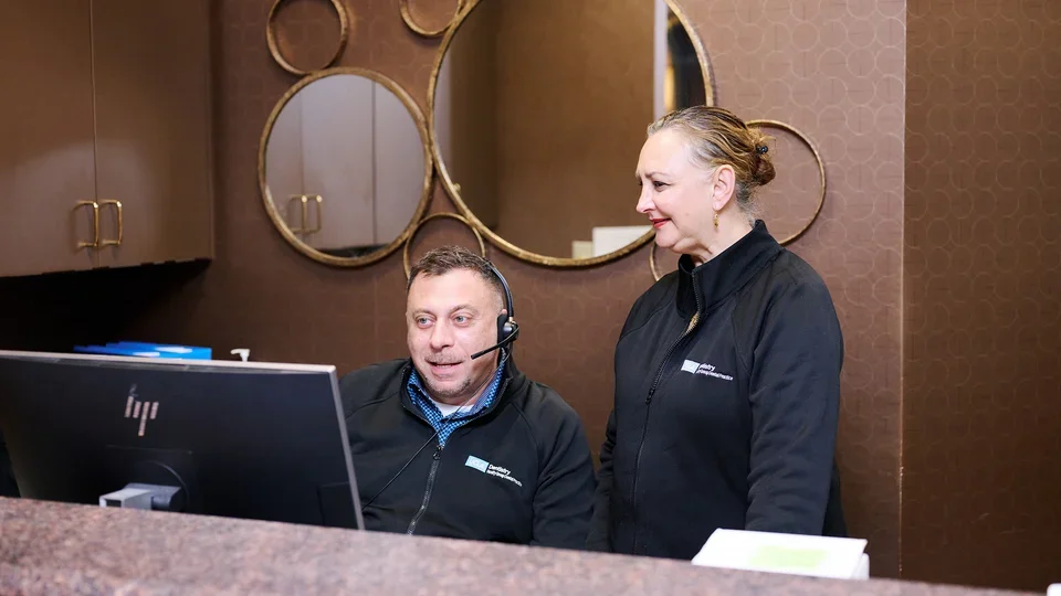 Two UCLA Faculty Group Dental Practice staff members are working at a reception desk in a professional office setting.