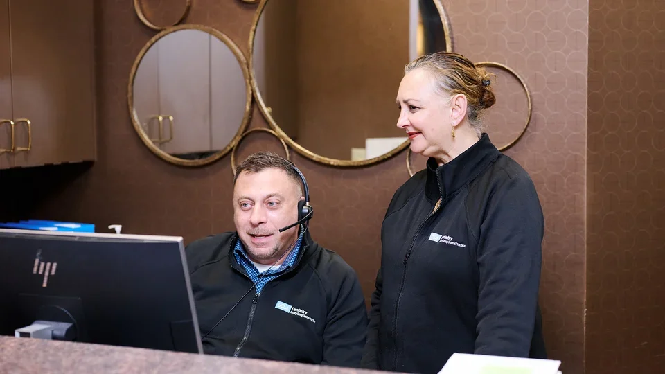 Two UCLA Faculty Group Dental Practice staff members are working at a reception desk in a professional office setting.