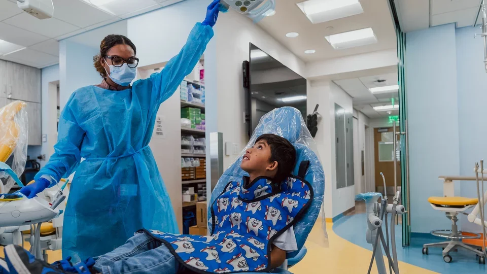 A pediatric dentsit adjusts a light above a patient in a chair