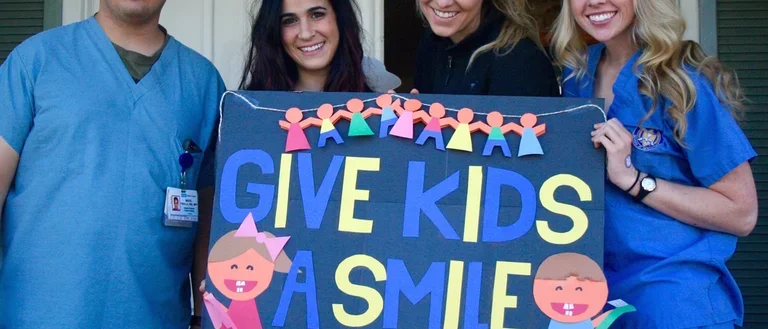 Students holding up give kids a smile sign