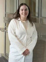 Amy Baks in a white lab coat, standing with hands clasped