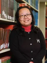 Yan Wang standing in a library, representing academic research, scholarship, and dental education resources.