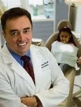 Dr. Ramos wearing a white coat with a child on a dental chair in the background