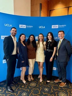 Six people smiling in front of UCLA backdrop