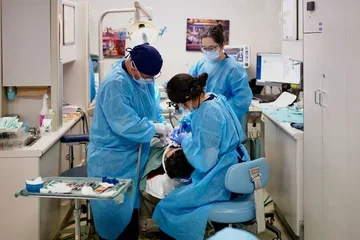 Three dentists in blue scrubs, treating a sedated patient