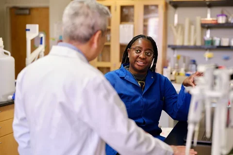 Lab researcher in blue coat explaining work to professor in white coat