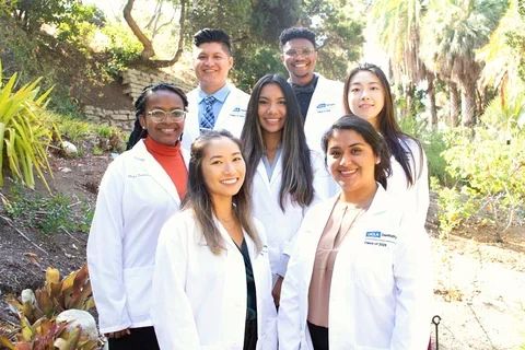 Seven people in white medical coats, standing in a botanical garden.
