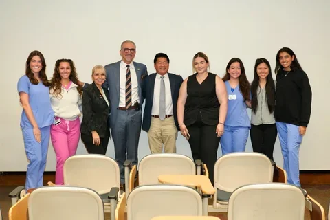 Group of nine people, some in medical scrubs and some in business attire, posing and smiling
