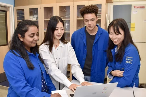 Four people in a laboratory, huddled around a laptop
