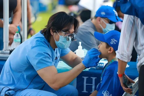 student dentist performing exa on child in a blue baseball cap