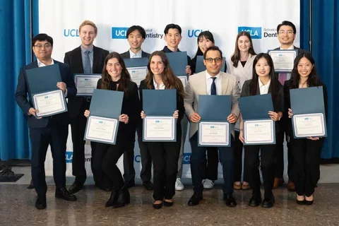 Group of 12 people holding award certificates, in front of UCLA School of Dentisrty-branded banner