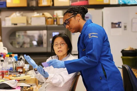 Two researchers, one in white lab boat, one in blue, collaborating in a lab