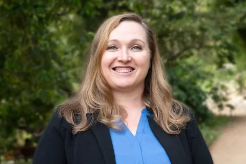 Dr. Owens is dressed in a black blazer layered over a blue blouse