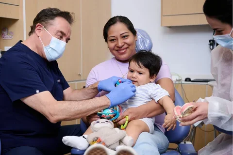 Dr. Francisco Ramos-Gomez administering care to a toddler patient seated on his mother's lap
