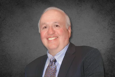 Dr. Peter Polverini smiling and wearing a dark pinstripe suit against a gray background
