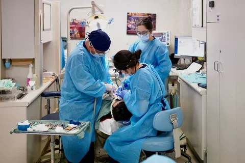 Three dentists in blue scrubs, treating a sedated patient