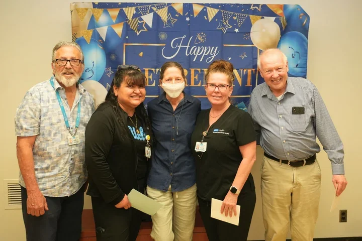 five people smiling in front of "happy retirement" sign