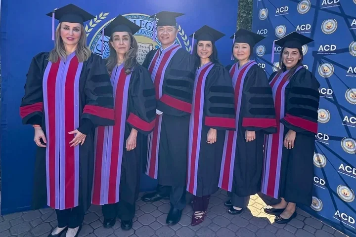 Six people in black graduation regalia against a blue backdrop