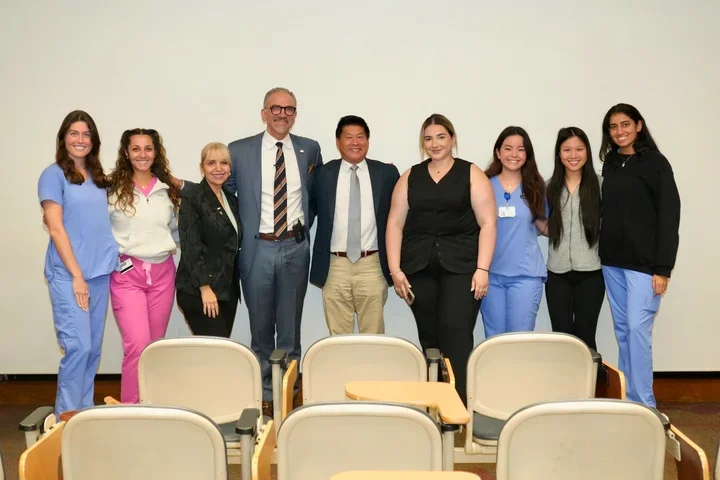 Group of nine people, some in medical scrubs and some in business attire, posing and smiling