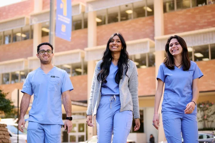 Three smiling students in medical scrubs outside the UCLA School of Dentistry