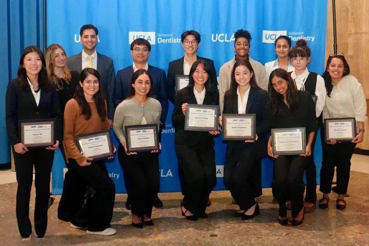 15 people smiling in front of a blue backdrop
