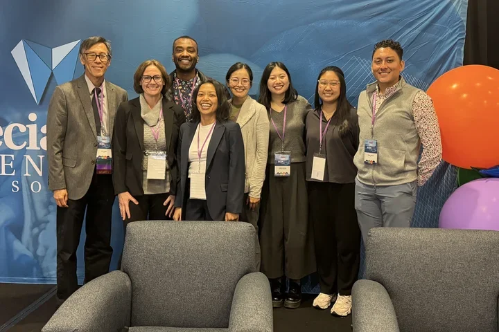 A group of eight people poses in front of a blue backdrop