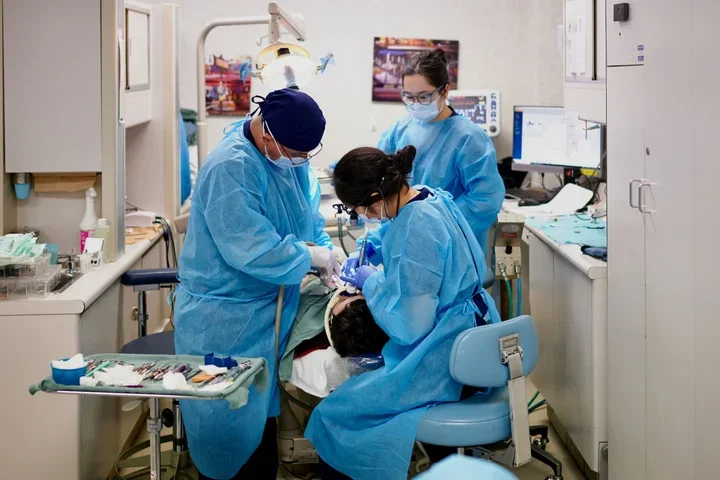 Three dentists in blue scrubs, treating a sedated patient