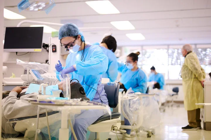 Dental students are treating patients in the UCLA School of Dentistry General Clinic while clinical faculty observe them.