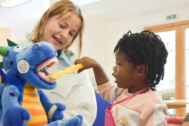 Woman showing child how to brush teeth using a stuffed animal
