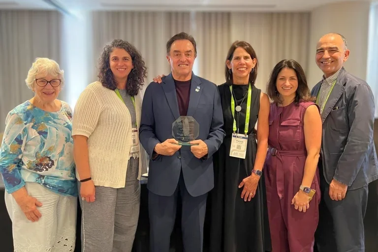 six people in business attire, with man at center holding an award
