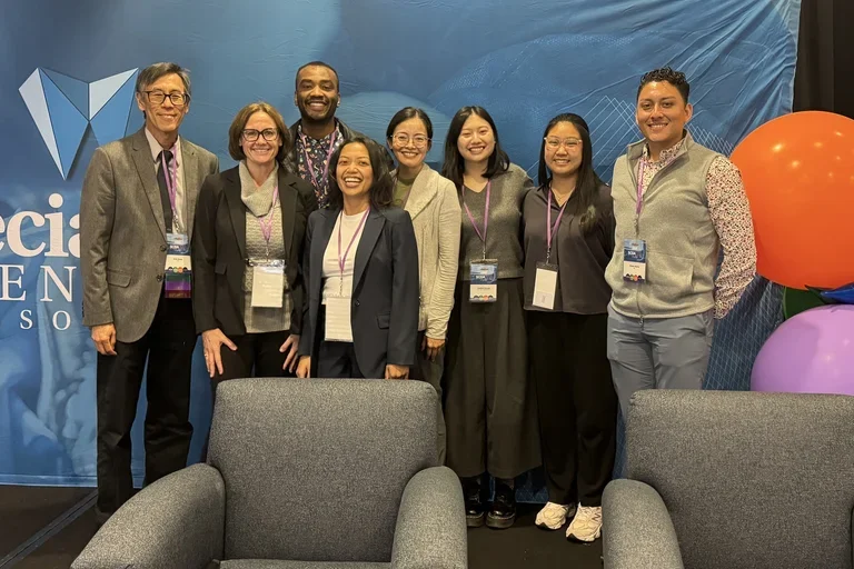 A group of eight people poses in front of a blue backdrop