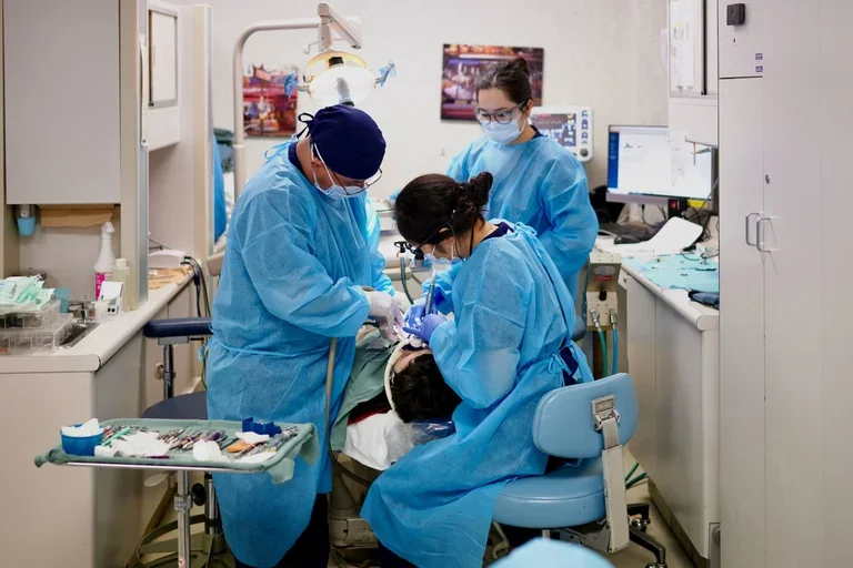 Three dentists in blue scrubs, treating a sedated patient