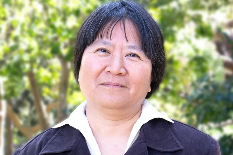 Dr. Yi-Ling Lin is wearing a blouse and a jacket in an outdoor setting.