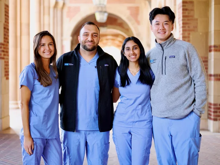 Four UCLA dental students smiling against a brick background