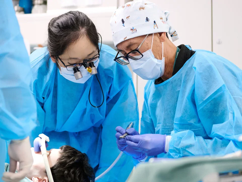 Dental Resident observing Dental Teacher working while patient is laying on chair with nitrous oxide mask over nose. 