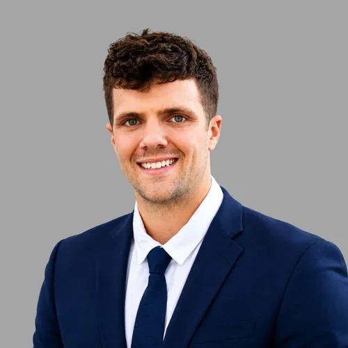 Rance Lockhart smiling, with short brown hair, wearing a navy suit, white shirt, and dark tie against a gray background.