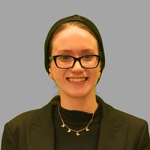 Medina Kerdjani, smiling, wearing glasses, a black headscarf, and black top against a gray background.