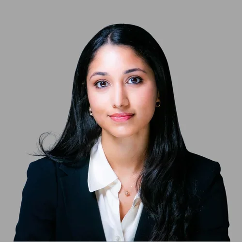 Praneetha Inampudi with long dark hair, wearing a dark blazer over a white collared shirt against a gray background.