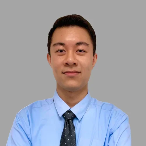Ryan Tran with short dark hair and glasses, wearing a light blue shirt and dark tie against a gray background.