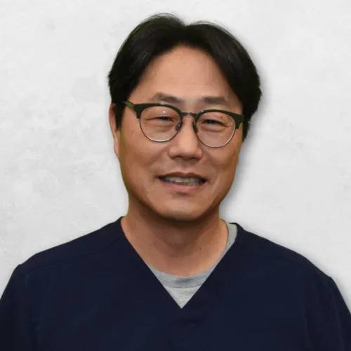 Dr. Kim is wearing navy blue scrubs and has glasses