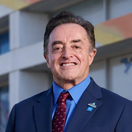 Francisco Ramos-Gomez smiling in a navy blue suit, standing in front of a building